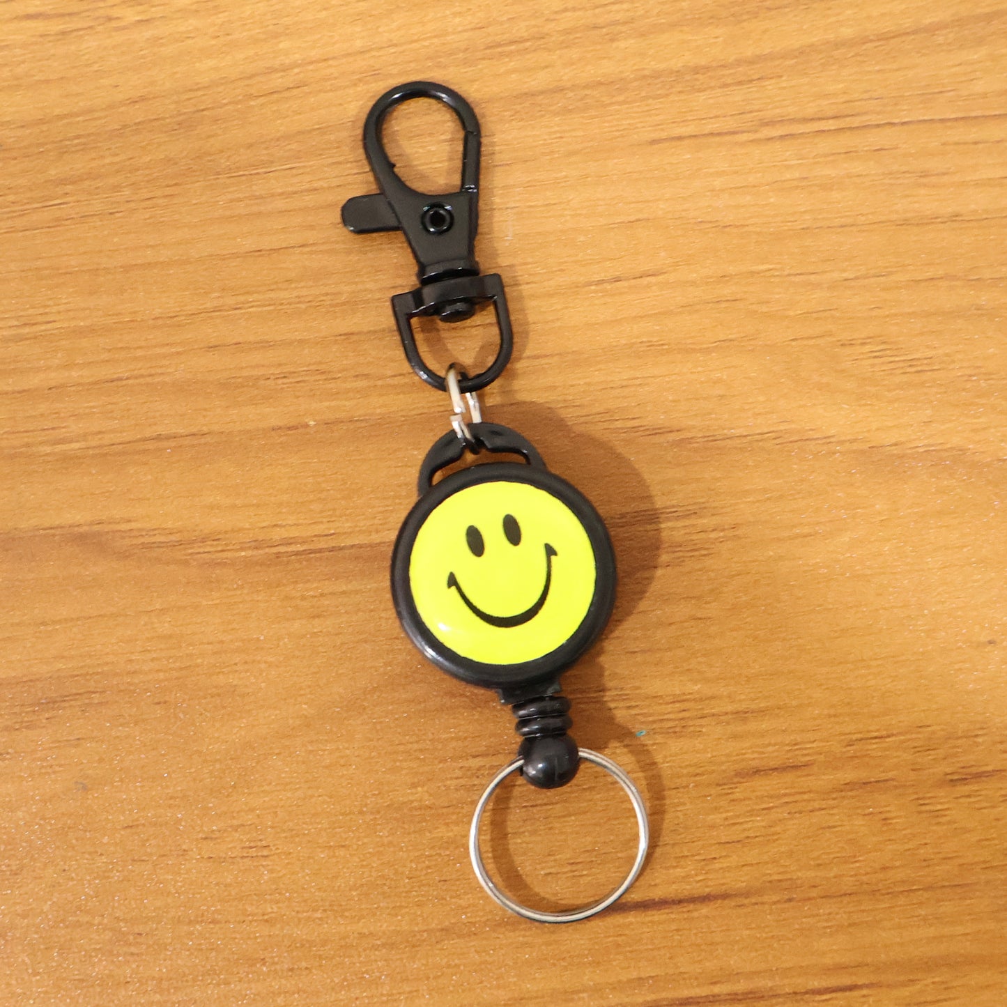 Wukusy smiley face retractable keychain displaying a cheerful yellow smiley with a metal clip for keys or accessories.