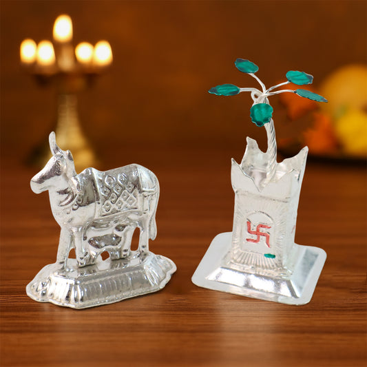 Silver-plated Kamdhenu cow pair with Tulsi plant for pooja and home decor, displayed on a wooden surface with traditional accents.