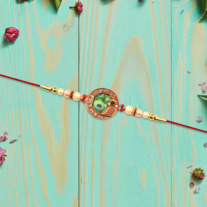 Elegant Wukusy Rakhi with peacock feather design, pearl beads, on red thread, perfect for festive celebrations.
