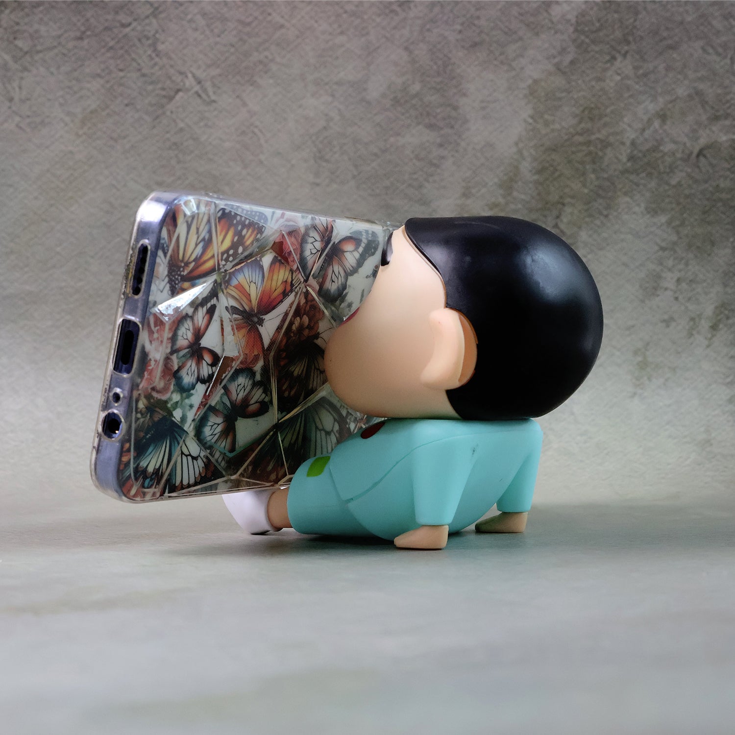 Wukusy cute cartoon figurine mobile phone stand on a desk, featuring colorful, whimsical character design for holding a smartphone.