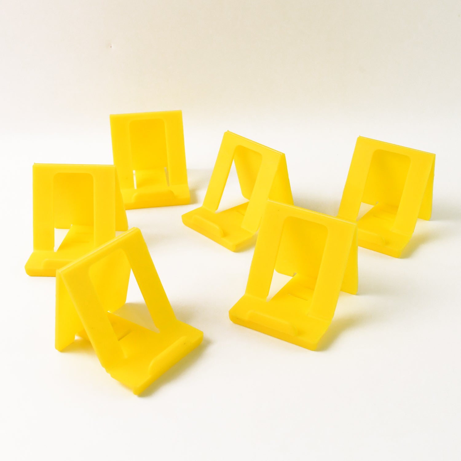 Six Wukusy adjustable foldable plastic mobile phone stands in mixed colors, shown folded and extended for hands-free viewing.