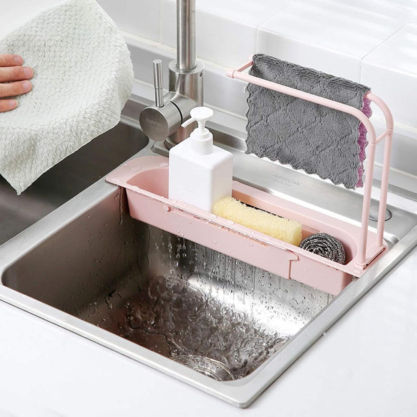 Wukusy kitchen sink organizer rack with towel holder and drain tray, shown holding utensils and cleaning tools in a modern kitchen setting.