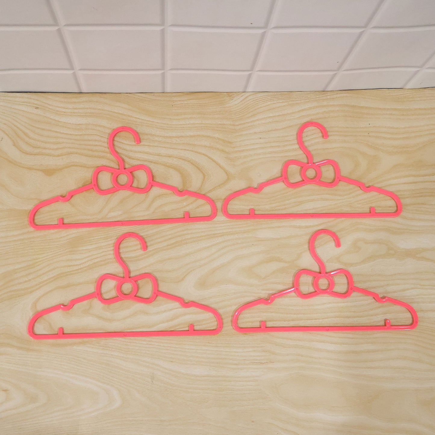 Set of four Wukusy kids plastic clothes hangers with cute bow designs for baby wardrobes, colorful and lightweight.