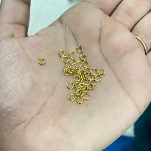 Golden open jump rings for jewelry making, Ekom brand, arranged in a pile, showcasing their small, circular metal design for crafts and jewelry.