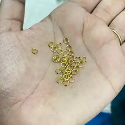 Golden open jump rings for jewelry making, Ekom brand, arranged in a pile, showcasing their small, circular metal design for crafts and jewelry.