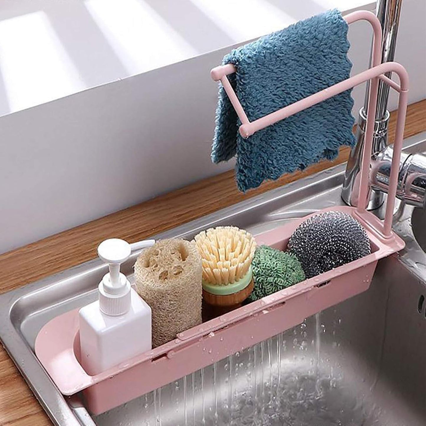 Wukusy kitchen sink organizer rack with towel holder and drain tray, holding sponges and utensils on a kitchen countertop.