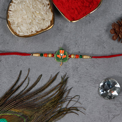 Green Tulsi leaf Rakhi with orange enamel flower and beaded thread, showcasing traditional Indian fashion jewelry.