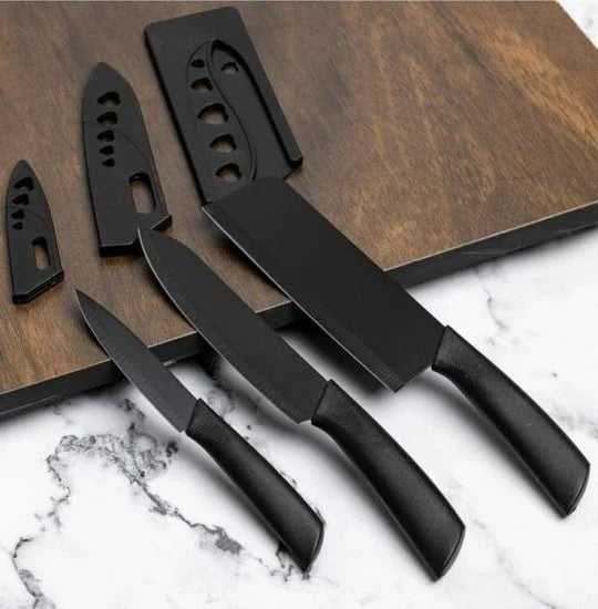 Set of three FIZZI SHOP JK SIDHU kitchen knives with black handles and stainless steel blades on a wooden cutting board.