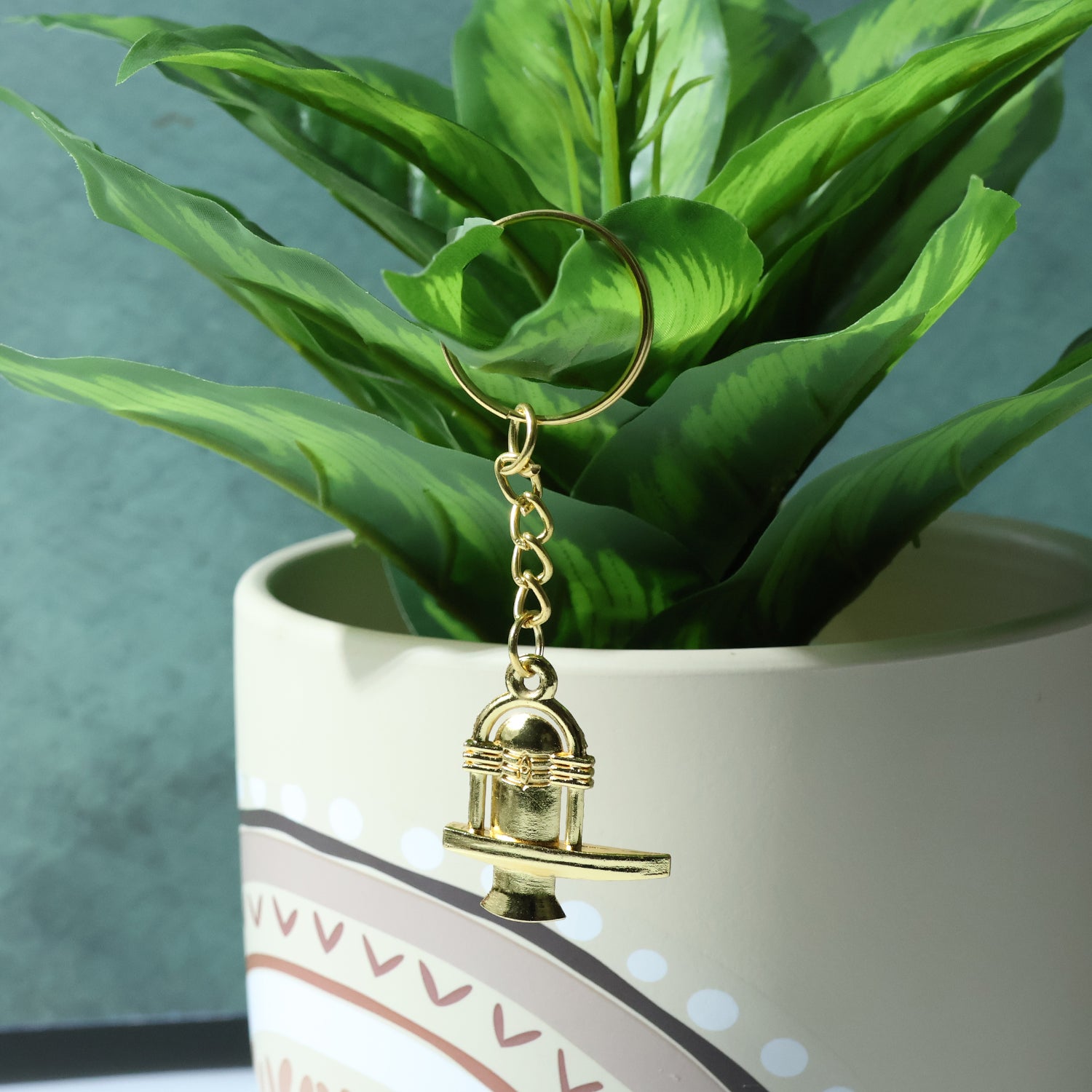 Golden metal Shivling keychain with intricate design, attached to a keyring, by Wukusy.