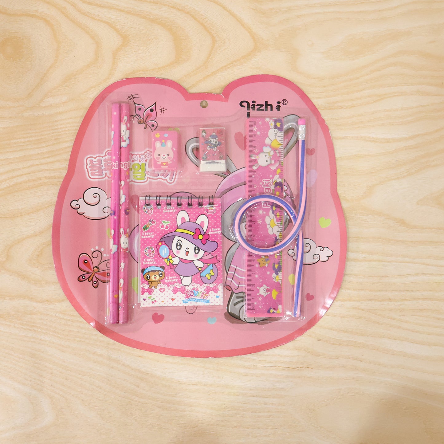 Wukusy 7-in-1 pink stationery set with ruler, pencil, eraser, notebook, and sharpener arranged on a desk.