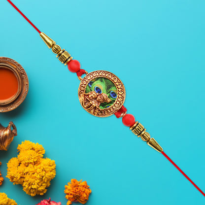 Traditional Krishna Rakhi with peacock feather design, decorative beads, on red thread, from Wukusy, showcasing intricate craftsmanship.