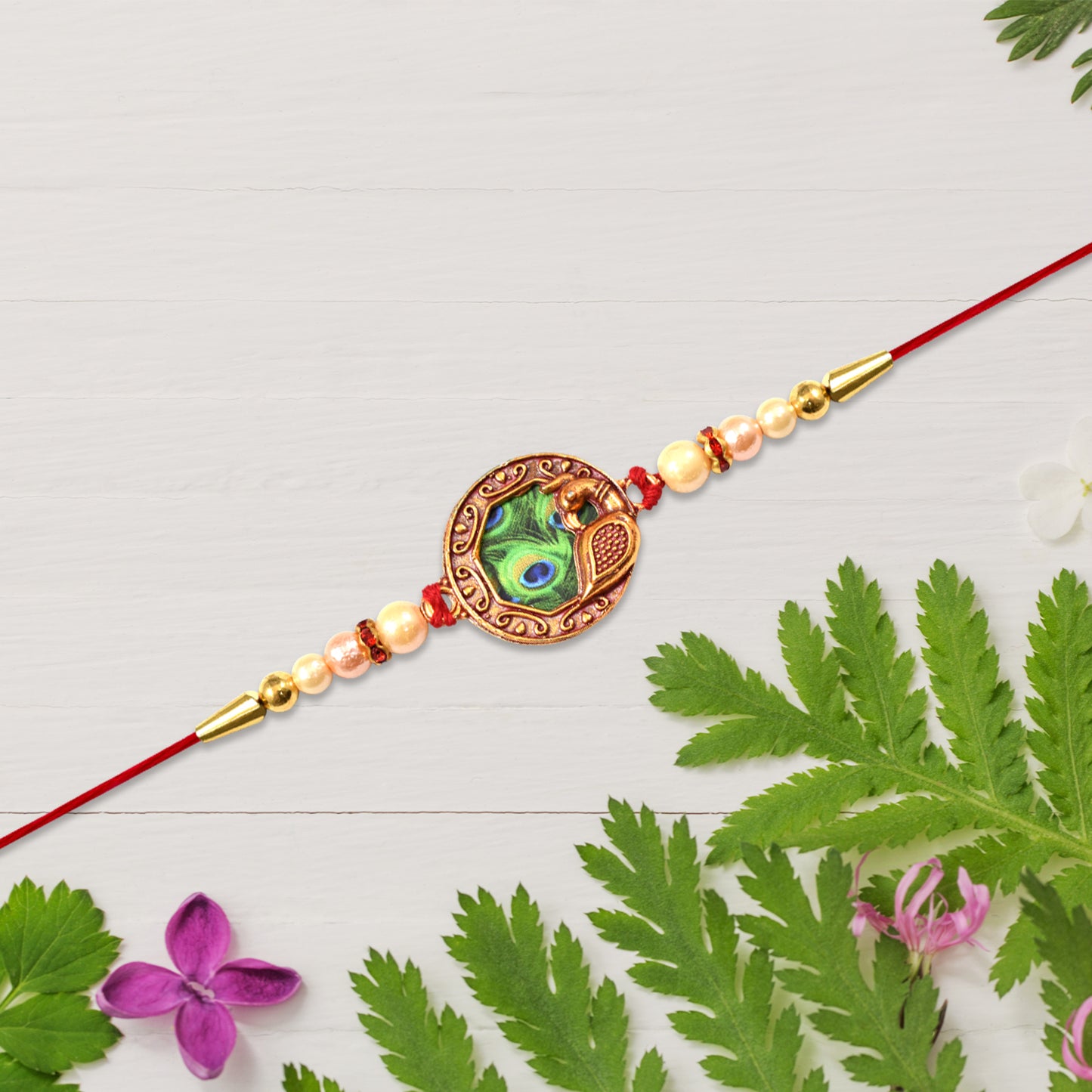 Elegant Wukusy rakhi with peacock feather design, pearl beads, and red thread for festive celebrations