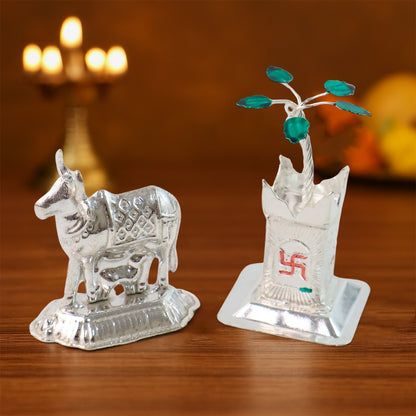 Silver-plated Kamdhenu cow pair with Tulsi plant for pooja and home decor, displayed on a wooden surface with traditional accents.